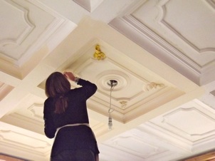 In this photo Jane stands atop a step ladder to add a gilt finish to ceiling mounted fleur-de-lis